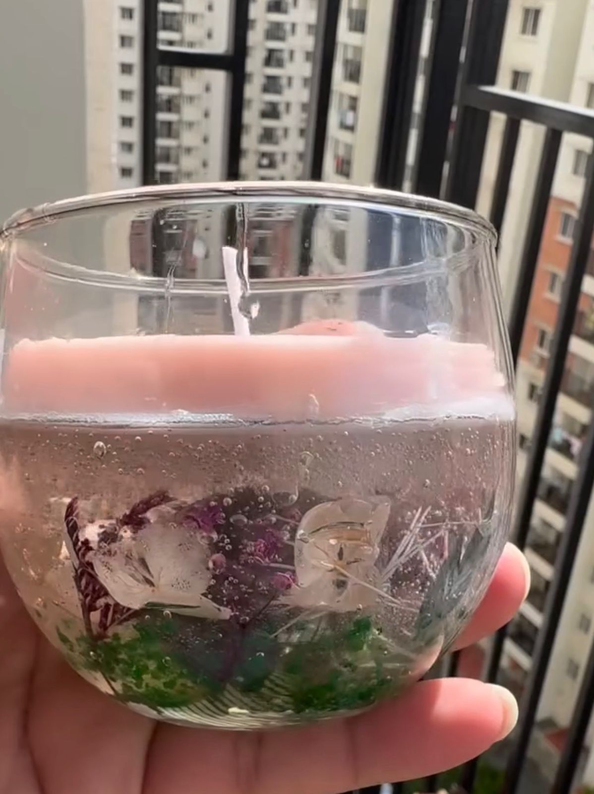 forest theme gel candle with dried flowers green base and pink wax top in clear glass cup